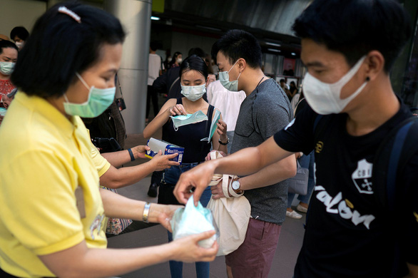 Nhân viên y tế phát khẩu trang cho người dân tại một ga tàu Skytrain ở Bangkok - Ảnh: REUTERS